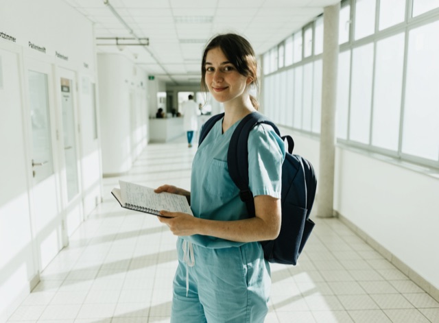 Junge Pflegekraft mit Rucksack und Notizbuch in einem hellen Klinikgang